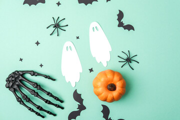 Halloween decorations with pumpkin, skeleton hand, ghosts, bats, and spiders on a teal background