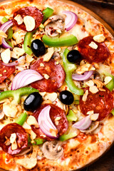 Pizza with chorizo ​​sausage, mozzarella cheese, green pepper and black olives. Rustic wooden background. Soft focus.	