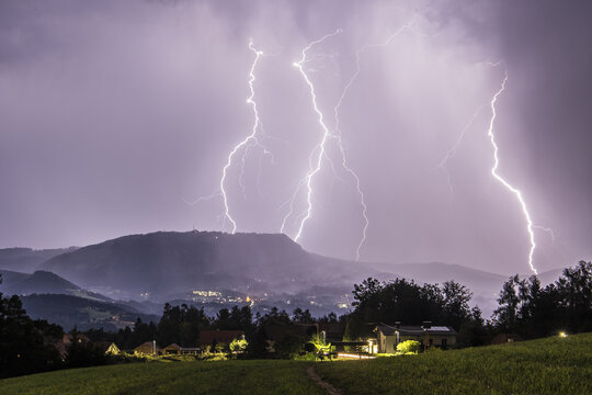View of jagged lightning bolts illuminate the sky over rolling hills and quaint houses, casting an ethereal glow on the landscape, Graz, Styria, Austria.