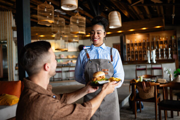 Waitress delivers a juicy burger in cozy restaurant setting with a warm smile and great hospitality