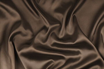 Fototapeta premium Crumpled, wrinkled brown colored glossy silk satin texture. Shiny smooth fabric with soft folds, cloth with wave drapery. Elegant and rich background, wallpaper, backdrop. Flat lay, top view