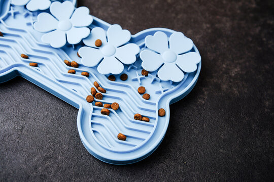 Blue bone shaped snuffle mat with kibble for dogs in a textured surface.
