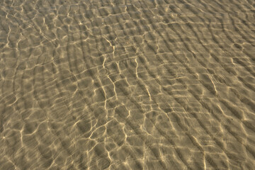 Transparent sea water. Sea water surface background. Sea shallows with visible sand at the bottom