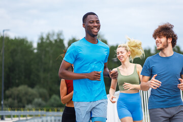 Smiling group of people running together on outdoor road.