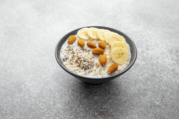 Healthy oatmeal with banana almond and chia seeds in dark bowl on gray table