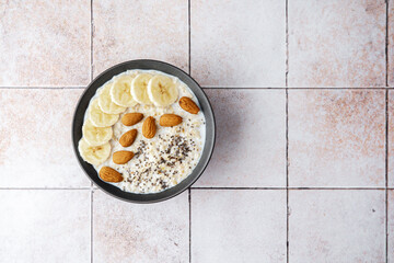 Banana almond chia oatmeal bowl with milk on white ceramic tile background