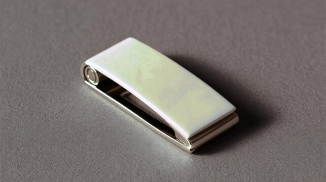 Small, rectangular-shaped money clip lying on a gray surface. the money clip is made of metal and has a silver finish. it has a rectangular shape with a flat top and a curved bottom.