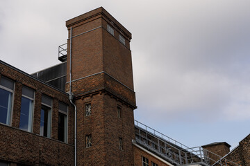 Stock photo of a vintage brick building exterior with a tower against a cloudy sky. Perfect for architecture, industrial, and urban themes.