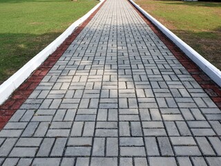 A straight walkway paved with interlocking grey bricks and a red border, creating a strong leading lines effect. The path is flanked by a lush green lawn, conveying a sense of direction and balance.