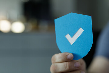 Image of a hand holding a blue shield with a checkmark, symbolizing security and approval.