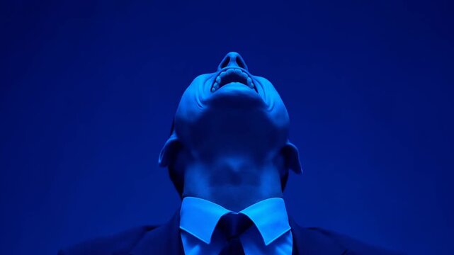 A man in a suit, lit in blue, screams with his hands raised
