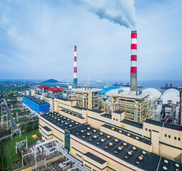 High angle view of a modern coastal power generation plant with towering red and white smokestacks...