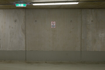 Stock photo of a plain concrete wall in a parking garage. Features an exit sign and no parking sign.