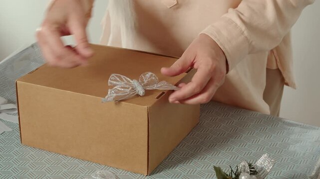 Woman attaching decorative bow to cardboard gift box