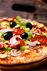 Pizza with chorizo ​​sausage, mozzarella cheese, green pepper and black olives. Rustic wooden background. Soft focus.	