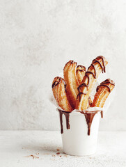 Minimalist photo of a white paper cup filled with churros drizzled with chocolate sauce. Light tones and clean background with copy space make it perfect for dessert, snack, or street food concepts.