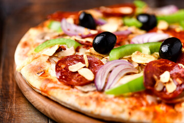 Pizza with chorizo ​​sausage, mozzarella cheese, green pepper and black olives. Rustic wooden background. Soft focus.	