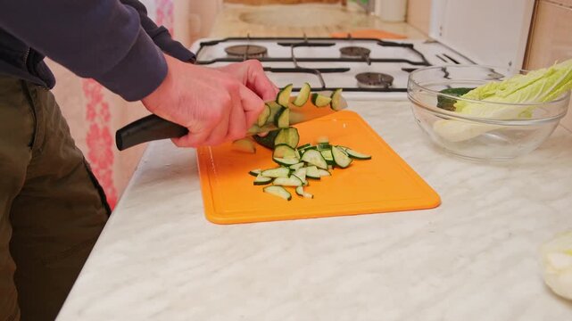 Man is cutting cucumber for a salad. Close up