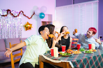 Playful moment as joyful friends laugh and feed each other fried chicken at a festive indoor dinner table, celebrating together with food, fun, and red party cups.