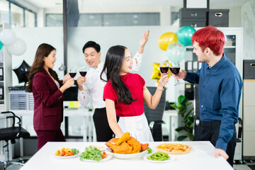 Energetic coworkers cheer with red wine at a lively office party table, celebrating teamwork, success, and joy with food, laughter, and festive decorations.