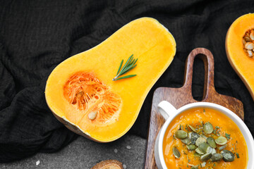 Butternut squash soup with pumpkin seeds and fresh rosemary on a cutting board with halved squash.