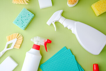 Cleaning supplies, sponges and brushes scattered on green background for household chores and tidy up
