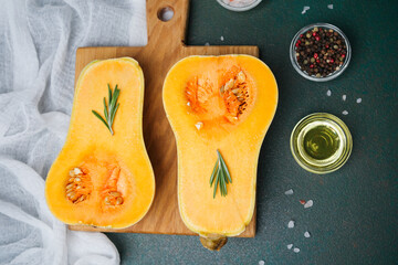 Butternut squash halves with rosemary, oil, and spices on a cutting board, top view.