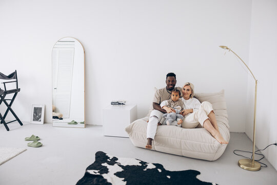 Happy african man and caucasian woman sitting on sofa with their biracial toddler daughter in room. - Powered by Adobe