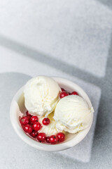 Vanilla ice cream scoops in bowl with fresh red currants on light background