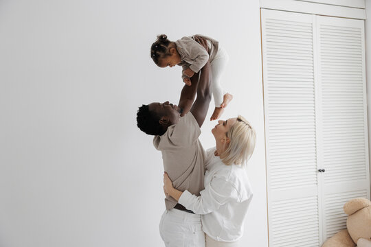 Happy biracial family with parents lifting their baby daughter high in the air, having fun together. Concept of interracial family. - Powered by Adobe