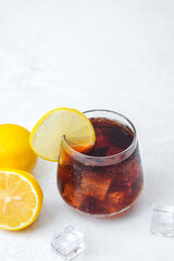Dark soda with lemon slice and ice cubes served in glass on bright background with citrus garnish