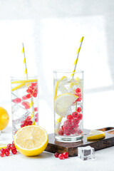 Two tall glasses with lemon red currant water and yellow striped straws on white table