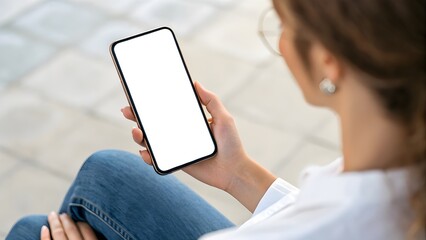 Close-up over the shoulder view of a woman holding a smartphone with a blank white screen, ideal for a website or mobile app display mockup