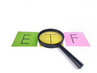 The word ETF is written on colorful note paper, viewed through a magnifying glass isolated on white...