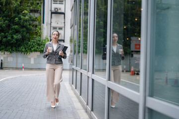 Confident businesswoman walking in the city while holding coffee and a laptop.