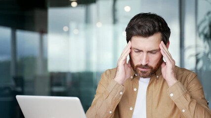 Businessman has depression suffering from mental pain sitting at workplace in office. Sad male holds his head with his hands, has personal problems, worries, feels despair, disappointment. Close up