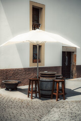 Rustic outdoor seating setup with a wooden barrel table, vintage stools, and a large white umbrella...