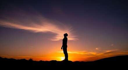 Silhouette of a person standing on a hilltop, gazing upwards at a vibrant sunset.