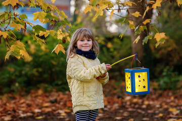 Little preschool kid girl holding selfmade traditional lanterns with candle for St. Martin procession. child happy about children and family parade in kindergarten. German tradition Martinsumzug