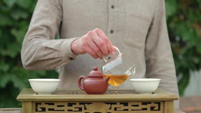 Cropped shot of a man standing behind chaban, pouring tea from glass chahai into two white tea cups.