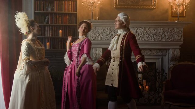Medium full shot of young 18th century Caucasian gentleman in red frock coat, breeches, lace jabot, wig visiting two noble ladies in mansion, greeting, bowing and kissing their hands