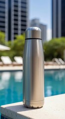 Fototapeta premium Stainless steel reusable water bottle stands by a blue swimming pool in a summer resort for hydration and sustainable living