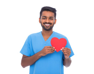 A smiling young Indian male medical professional in blue scrubs holds a vibrant red paper heart, symbolizing health, love, and dedicated care isolated on a transparent background