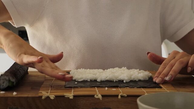 A woman skillfully prepares sushi in her kitchen, focusing on rolling rice and seaweed with precision. Discover helpful tips and techniques for making sushi at home
