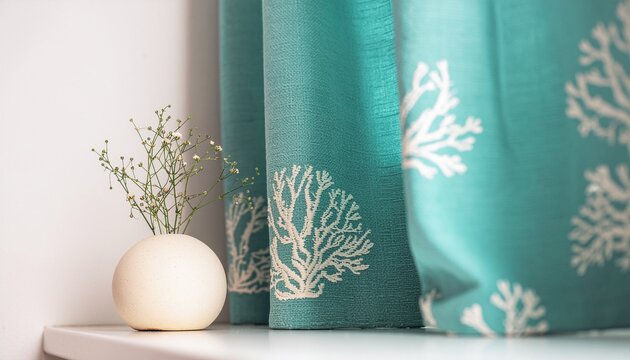 Close up of a delicate white coral branch pattern on flowing teal turquoise fabric curtains with a small white vase holding a sprig of baby s breath flowers on a white shelf