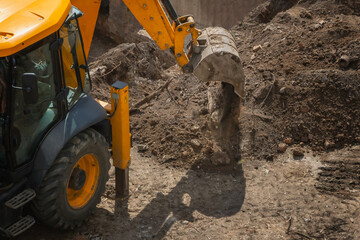 Excavator at construction site performs earthworks dumping soil from bucket on hot sunny day,...