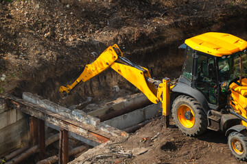 Excavator bucket operates as crane for extraction and replacement of water pipes at construction site during repair works of public utilities