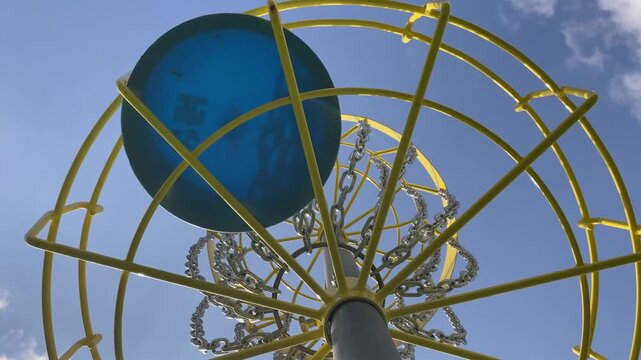 Disc golf basket with metal chains. Blue frisbee hits the target. View from below the basket.