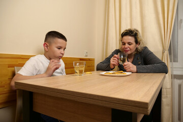 Mother and son sitting at table, drinking tea and eating cookies, sharing warm family interaction and quality time together.