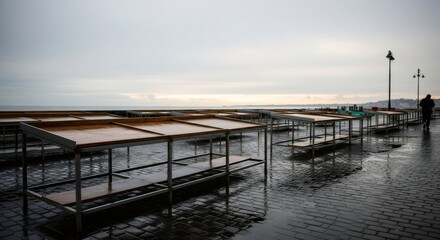 Obraz premium Abandoned seaside market stalls on rainy day. Empty waterfront promenade with wet pavement. Melancholic coastal scene. Nostalgic 80s-90s atmosphere. Retro vhs style image